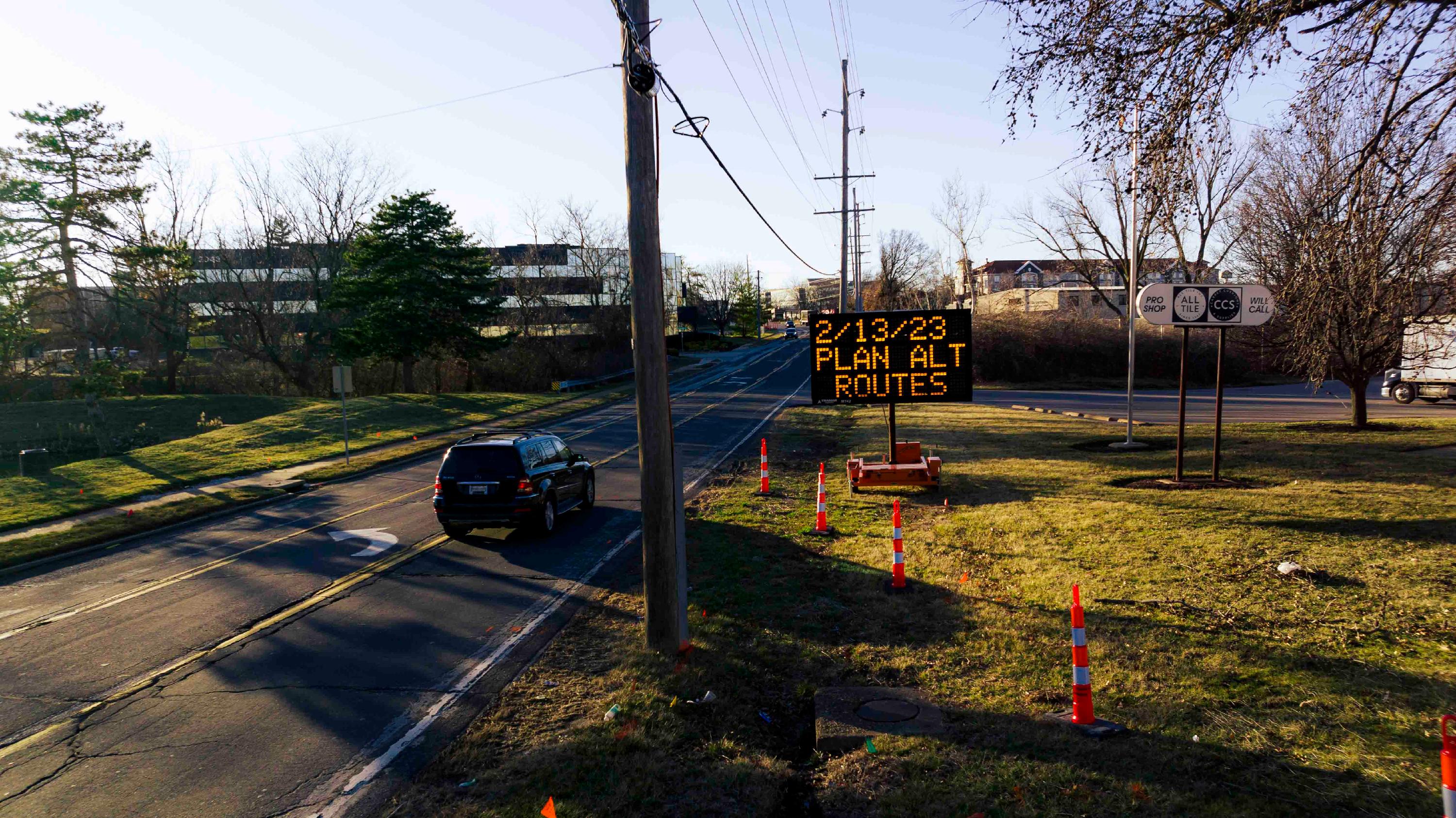 A car drives on Lackland Road as a sign reads "2/13/23 - Plan Alt Routes" in refrence to a scheduled maintenance closure